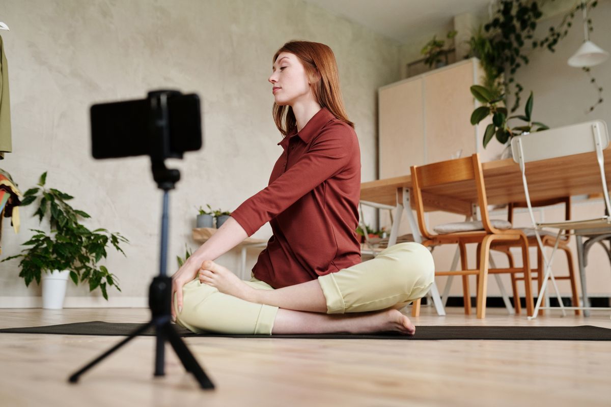 Yoga teacher recording a class at home with a phone on a tripod